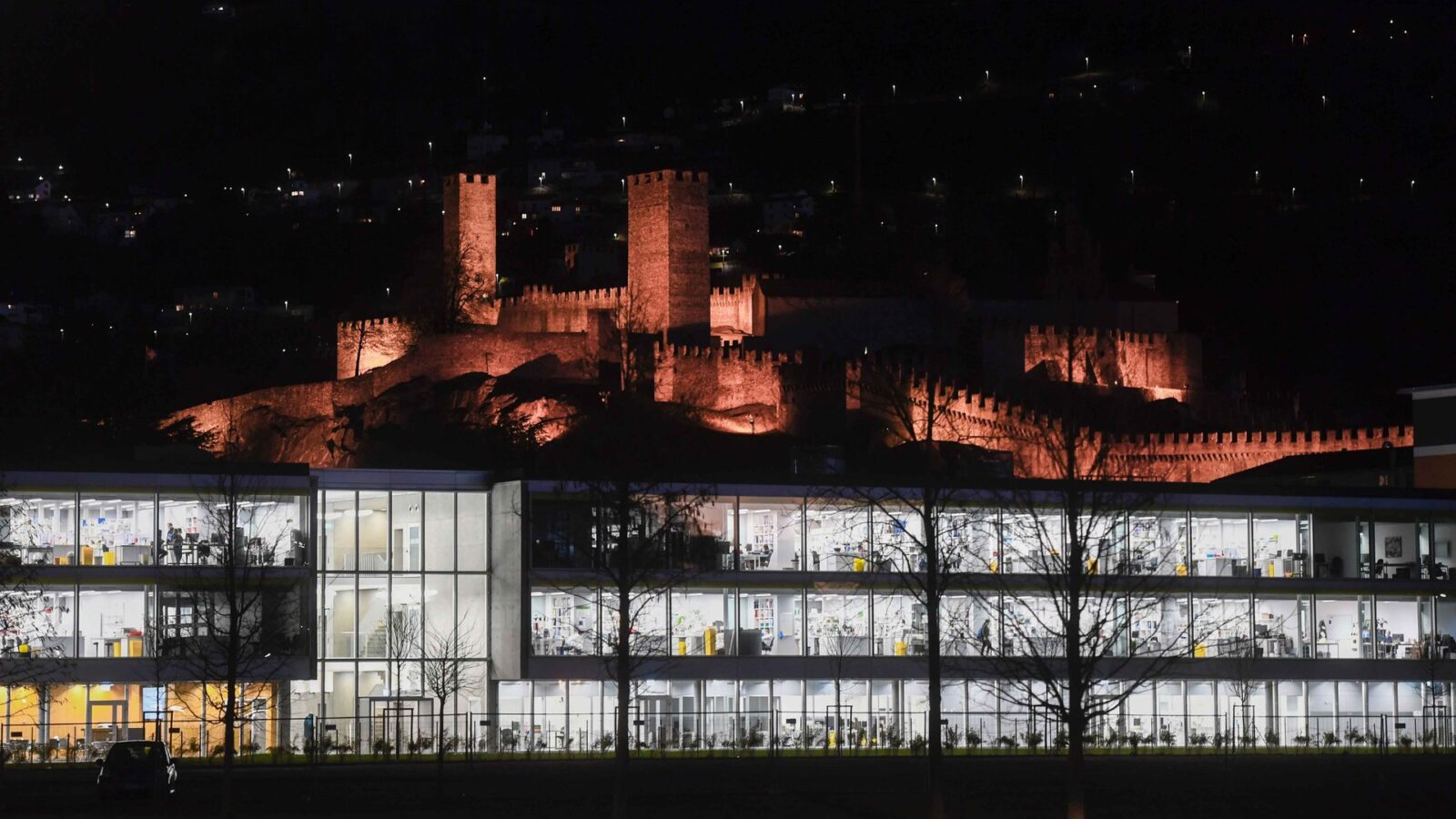 The USI Bellinzona Campus at night, with the illuminated castle above it