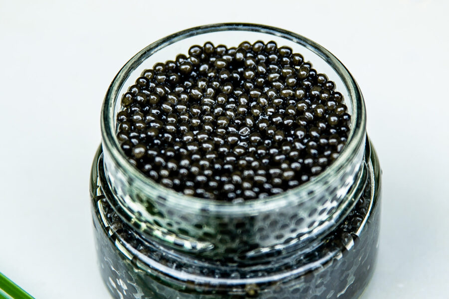 An open jar of fresh caviar with a green glass spoon