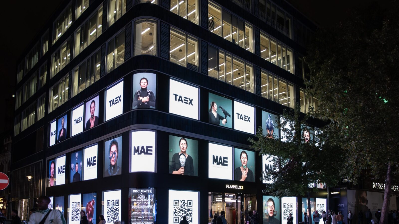 A building facade at night covered with TAEX and MAE digital portraits