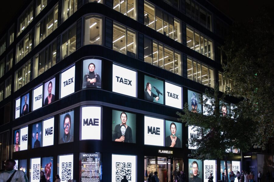 A building facade at night covered with TAEX and MAE digital portraits